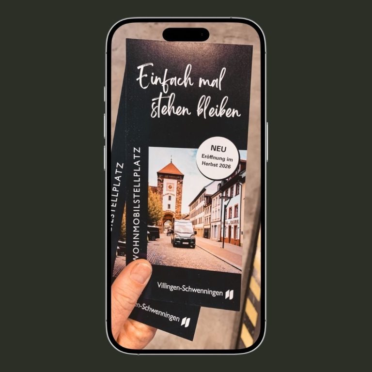 Fotoshooting für Wohnmobil-Stellplatz Eine Hand hält ein Smartphone mit einem Stadtführer und einem Bild einer Straße.