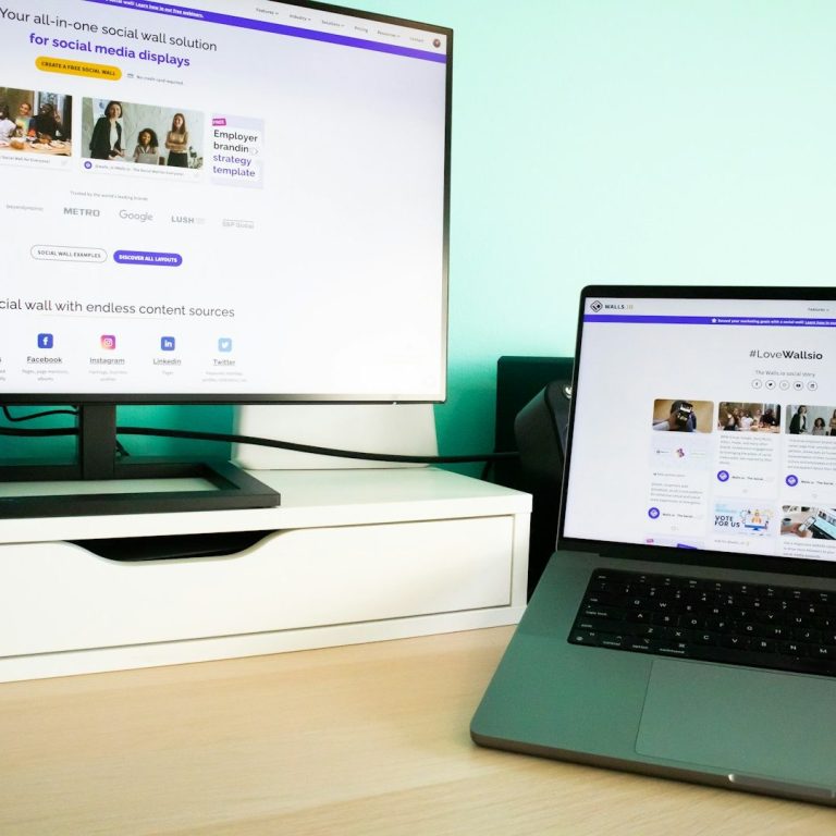 Umsetzung & Begleitung Schreibtisch mit einem Monitor und einem Laptop, beide zeigen Webseiteninhalte.