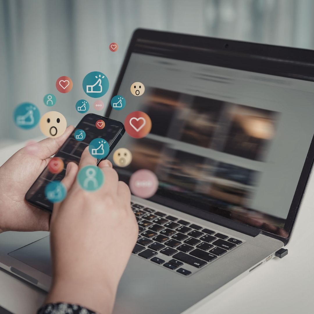 Social Media Management & Begleitung Hände mit Smartphone, umgeben von sozialen Medien-Icons, neben Laptop.