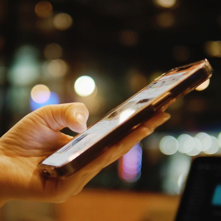 Eine Hand hält ein Smartphone mit hellem Bildschirm bei schwachem Licht.