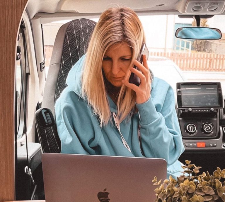 oliventure media sina Huck Frau im blauen Hoodie, die am Laptop arbeitet und telefoniert, sitzt in einem Van.